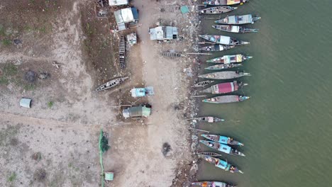 Toma-Aérea-De-Arriba-Hacia-Abajo-Que-Muestra-Barcos-De-Pesca-Estacionando-En-La-Cubierta-Junto-Al-Barrio-Pobre-Del-Gueto-En-Phnom-Penh.