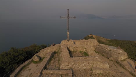 Cruz-De-Acero-Con-Detalles-De-Graffiti-Y-Lago-De-Garda-En-El-Panorama-Aéreo-De-Niebla