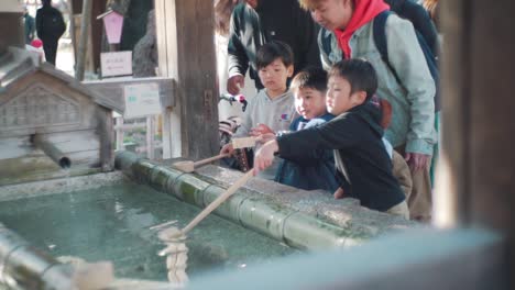 Children-Washing-Their-Hands-At-The-Temizuya-Before-Entering-At-The-Hirano-Jinja-Shrine-In-Kyoto,-Japan