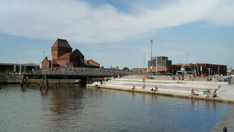 Menschen-Sitzen-Im-Sommer-Am-Wasser-Neben-Der-Alten-Brücke-In-Lübeck,-Weitwinkelaufnahme