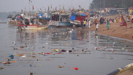 Primer-Plano-De-La-Contaminación-Del-Agua-Cerca-De-La-Orilla-Del-Mar,-Flores,-Plásticos,-Alimentos,-Botellas-Y-Desechos-En-La-Ciudad-De-Mumbai,-India,-Cerca-De-Pequeños-Barcos-De-Pesca-Atracados-O-Estacionados-En-La-Costa-Fondo-De-Video-En-Prores-422-Hq