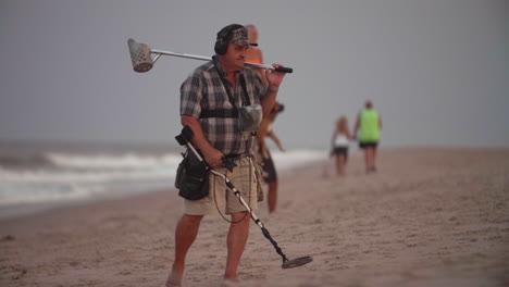 Hombre-Mirando-A-La-Cámara-Con-Detector-De-Metales-En-La-Playa