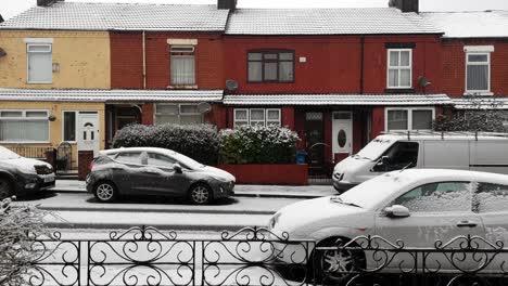 Idyllic-winter-snow-falling-in-empty-street-of-town-houses-and-parked-cars