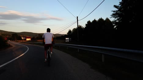 Ein-Junge-Fährt-An-Einem-Sommertag-Bei-Sonnenuntergang-Mit-Dem-Fahrrad-Auf-Einer-Landstraße