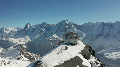 Drone-circling-skilift-building-with-terrace-on-top-of-snow-covered-mountain