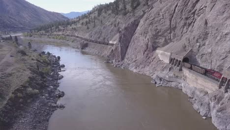 Descending-aerial:-freight-train,-suspension-bridge,-swirling-river