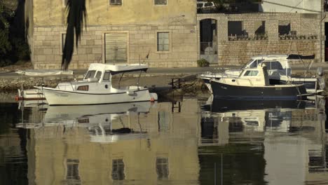 Un-Par-De-Barcos-Atracados-A-Lo-Largo-De-Una-Carretera-En-Vela-Luka-En-Croacia-Con-Un-Claro-Reflejo-En-El-Agua