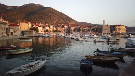 Vista-Panorámica-De-Komiza,-Sus-Numerosos-Barcos-Atracados-En-La-Cala-Y-El-Castillo-Al-Atardecer-Con-Suaves-Olas