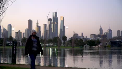 Eine-Frau-Mit-Maske-Geht-Während-Der-Globalen-Coronavirus-Pandemie-An-Der-Skyline-Einer-Stadt-Vorbei