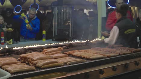 Menschen-Kochen-Würstchen-Auf-Einem-Grill-Auf-Einem-Weihnachtsmarkt-In-Hamburg,-Deutschland,-Im-Dezember-2019,-Mit-Menschenmengen,-Die-Im-Hintergrund-Essen