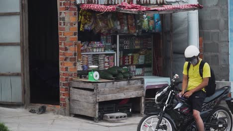 Boy-on-motorbike-with-helmet-and-protective-mask-near-typical-kiosk