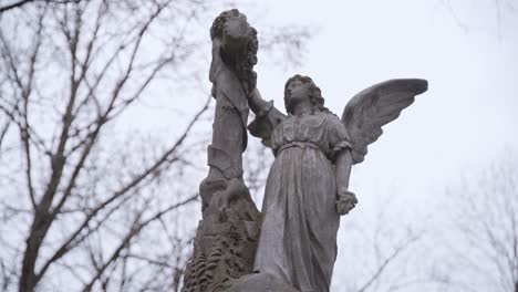 Old-Stone-Marble-Statue-of-Angel-with-Swinging-Tree-Branches-in-Background