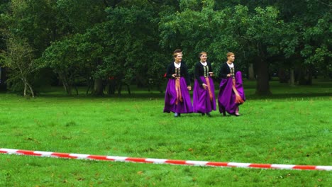 Adult-caucasian-female-dancers-in-traditional-folk-costumes-walking-over-the-green-field-before-a-dance-performance-in-open-air,-sunny-summer-evening,-happy,-Latvian-national-culture,-wide-shot