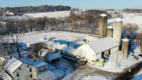 Luftschnee-Fällt-über-Landwirtschaftliche-Gebäude,-Felder-Mit-Weißem-Bodendecker