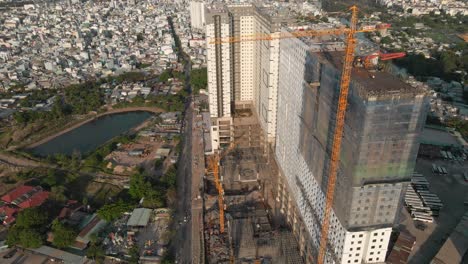 Drone-flying-backwards-with-camera-tilt-up-shows-a-building-under-construction-and-a-busy-road-with-many-motorists