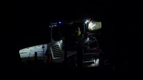 Hombres-Con-Uniforme-Reflectorizado-Hablando-Mientras-Están-Sentados-En-Una-Máquina-Pavimentadora-De-Carreteras-Por-La-Noche