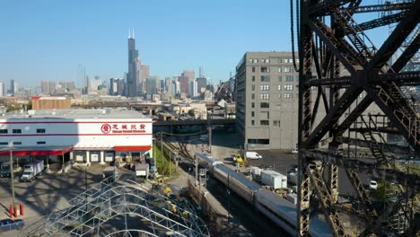 Birds-Eye-Aerial-View-of-Metra-Train-in-Chinatown,-Chicago-Cityscape-in-Background