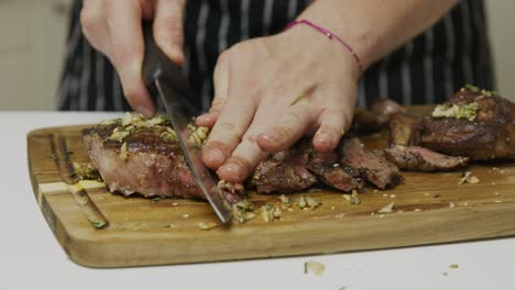 Primer-Plano-Sobre-El-Chef-Cortando-Bistec-De-Ternera-Recién-Cocinado-En-Una-Tabla-Cortada-De-Madera