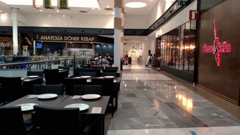 POV-Walking-Past-Empty-Restaurant-Table-And-Chairs-At-As-Cancelas-Shopping-Center-In-Galicia,-Spain