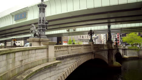 TOKYO,-JAPAN,-circa-April-2020:-cars-passing-and-pedestrians-walking-on-historical-Nihonbashi-bridge-over-the-river,-highway-overhead,-at-old-downtown-in-central-financial-area,-day-time