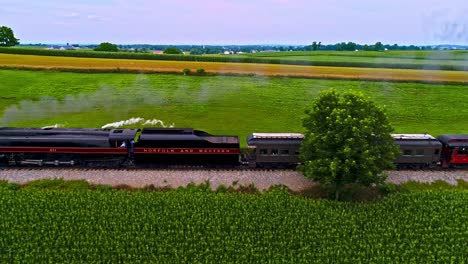 Una-Vista-Aérea-Paralela-De-Un-Antiguo-Tren-De-Pasajeros-De-Vapor-Que-Sopla-Humo-Negro-A-Través-De-Las-Tierras-Agrícolas-De-Pensilvania