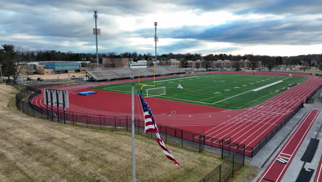 Amerikanische-Flagge-Weht-Im-Wind-Auf-Dem-Sportlichen-Fußballplatz,-Luftaufnahme-Des-Stadioncampus