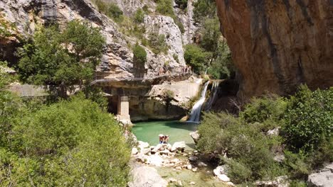 Alquezar-En-Huesca,-Aragón,-España---Caminata-Pasarelas-Del-Vero---Vista-Aérea-De-Drones-De-Turistas-Caminando-Por-El-Puente-Peatonal-Y-Nadando-En-La-Cascada