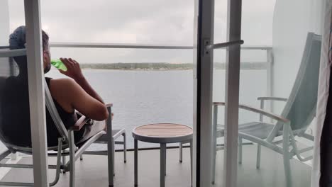 A-Young-Asian-man-having-a-sip-of-beer-in-balcony,-apartment-with-beautiful-ocean-view-in-background