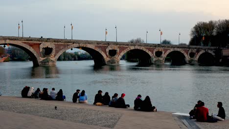 Junge-Leute-Genießen-Den-Sonnenuntergang-Am-Ufer-Der-Garonne-Vor-Der-Brücke-Pont-Neuf