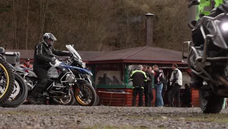 Motorrad-Crew-Startet-Reise-Vom-Parkplatz-Bahnhof-In-Zeitlupe,-Team-Extremer-Offroad-Biker-Reist-Mit-Voll-Ausgestatteten-Helmen-Und-Feuerfester-Kleidung-Zum-Abenteuer,-Gruppe-Verlässt-Position