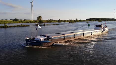 Aerial-Parallax-Shot-Off-The-Forward-Bow-Of-Amare-Inland-Motor-Freighter-Travelling-Along-Against-Still-Wind-Turbines-In-The-Background