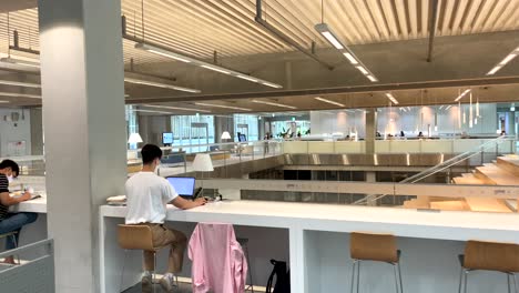 Schwenkaufnahme,-Die-Koreanische-Studenten-Mit-Gesichtsmaske-Zeigt,-Die-Mit-Laptop-Auf-Einem-Modernen-Bibliotheksgebäude-Sitzen-–-Arbeiten-Und-Lernen-Im-Asien-Kulturzentrum-Von-Gwangju