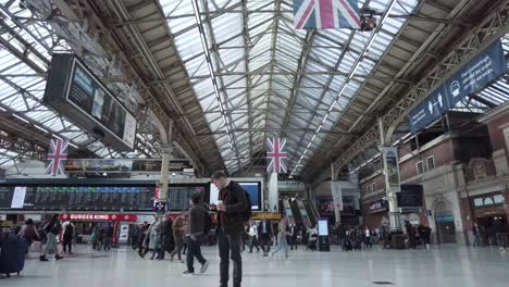 Vista-Interior-Mirando-Hacia-El-Techo-De-La-Estación-Victoria-De-Londres-Con-Los-Viajeros-Pasando