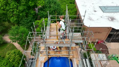 Female-blue-collar-construction-workers-fasten-and-paint-weather-vane-high-atop-scaffolding-during-church-renovation