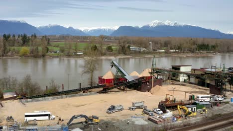 Camiones-Y-Cargadores-Que-Trabajan-En-La-Zona-Industrial-Con-Barcaza-De-Carga-De-Apiladores-Radiales-En-El-Río-Fraser