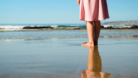 Reflejo-En-La-Arena-Mojada-En-La-Playa-De-Una-Chica-Con-Vestido-Rosa-Mirando-Las-Olas