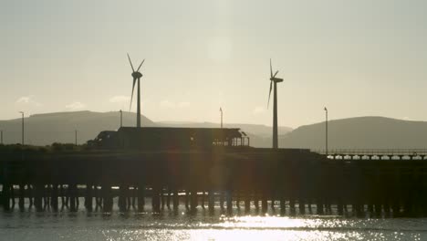 Hermosa-Toma-De-Turbinas-Eólicas-Girando-En-La-Iluminación-Del-Amanecer-Y-Sorprendentes-Destellos-Solares-Y-Reflejos-En-El-Agua-En-El-Puerto-Deportivo-De-Swansea-Uk-4k