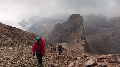 Some-climbers-climbing-a-rocky-mountain,-under-a-cloudy-sky-on-a-very-windy-day