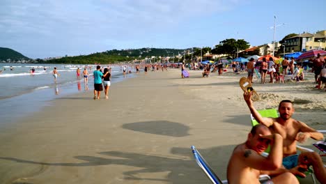 Dolly-in-of-people-having-fun-sitting-in-the-sand-near-the-seashore-in-Bombas-and-Bombinhas-beaches,-Brazil