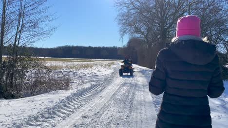 Ein-Mädchen,-Das-Auf-Einer-Verschneiten-Landstraße-Spaziert,-Trifft-Im-Winter-Einen-Mann,-Der-Ein-Geländefahrzeug-Fährt-Und-Mit-Kindern-Einen-Schlitten-Zieht