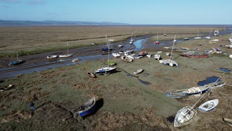 Various-weathered-abandoned-fishing-boat-wreck-shipyard-in-marsh-mud-low-tide-coastline-aerial-reverse-right-view