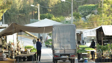 Ein-Straßenhändler-Hebt-Das-Zelt-Hoch,-Während-An-Einem-Sonnigen-Tag-Ein-Lastwagen-Am-Straßenmarkt-Vorbeifährt