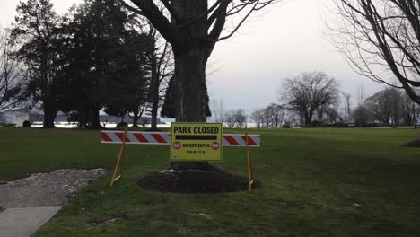 Park-Closed-Do-not-enter-signs-side-pan-across-front-entrance-of-park-with-trees-and-grassy-field