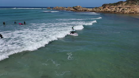 Orbiting-aerial-of-young-surf-student-catching-small-green-shore-wave