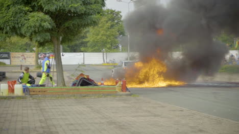 Car-Driving-With-Professional-Stuntman-Tied-And-Pulled-Behind,-Passing-By-Flaming-Ground-At-The-Arena