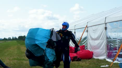 Professional-male-skydiver-taking-his-blue-parachute-after-a-successful-landing,-overcast-summer-day,-medium-handheld-shot