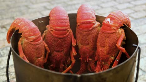 Four-spiny-lobster-hanging-in-steel-pot-after-being-cooked,-steam-escaping