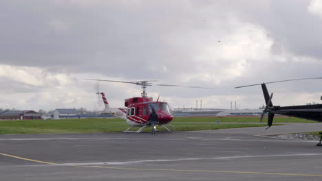 Man-Walking-Towards-Search-And-Rescue-Helicopter-At-The-Heliport-In-British-Columbia,-Canada-On-A-Cloudy-Day