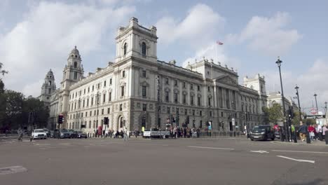 Panning-shot-of-motor-vehicles-crossing-the-busy-intersection-in-front-of-the-building-that-is-home-to-the-Cabinet-and-Her-Majesty's-Revenue-and-Customs-offices-in-Westminster,-London,-England