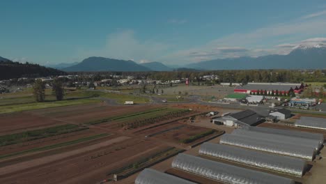 Granja-De-Cosecha-Local-En-Chilliwack-Bc-Campos-Marrones-Cultivos-Recién-Plantados-En-Primavera-Amplia-Inversión-Aérea-Revelando-Tráfico-árboles-Montañas-Valle-Nubes-Cielo-Azul-Día-Soleado